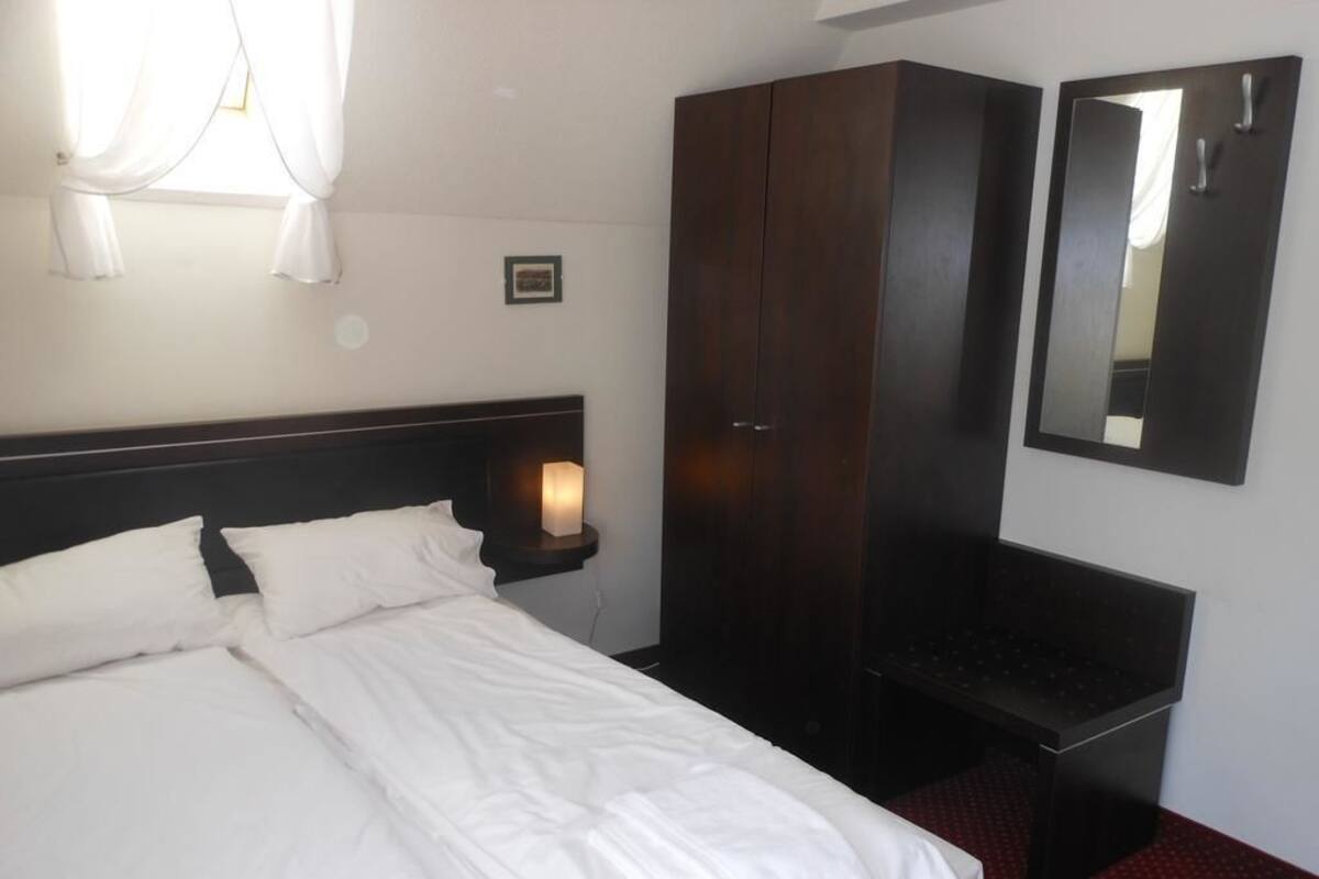 Una habitación de hotel con cama, armario, mesita de noche y espejo.