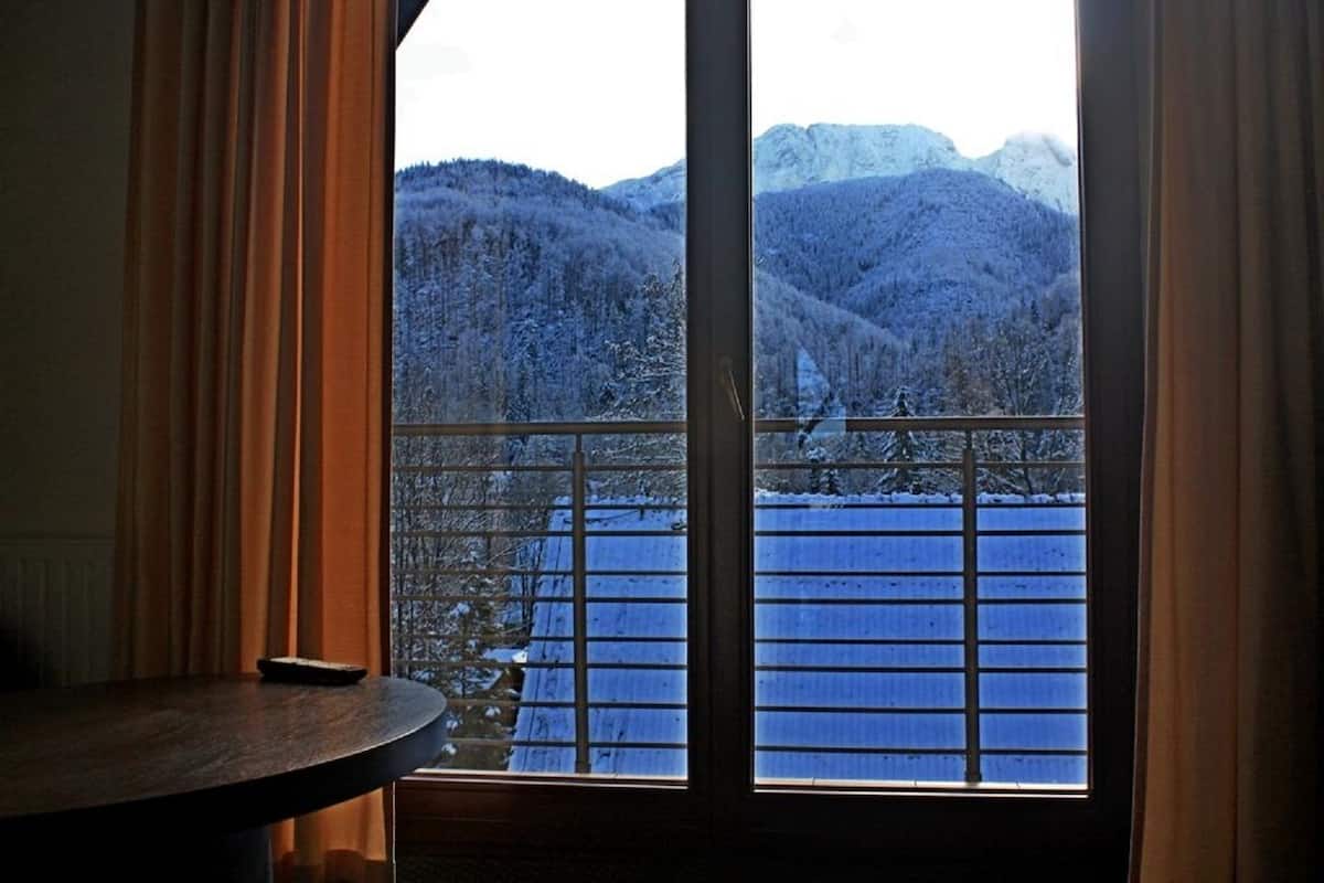 Una habitación con un ventanal que ofrece vistas a montañas nevadas y un edificio azul en el exterior.