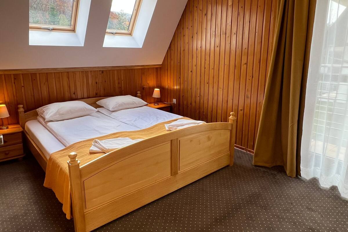 Un dormitorio con cama de madera, dos mesitas de noche y un ventanal con vistas a árboles.