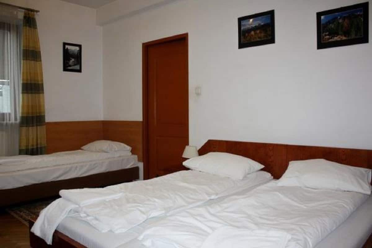 Habitación de hotel con dos camas individuales, cabecero de madera, una puerta y dos cuadros en la pared.