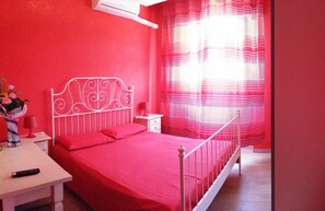 Una habitación con cama, mesita de noche, lámpara y ventana con cortinas a rayas.