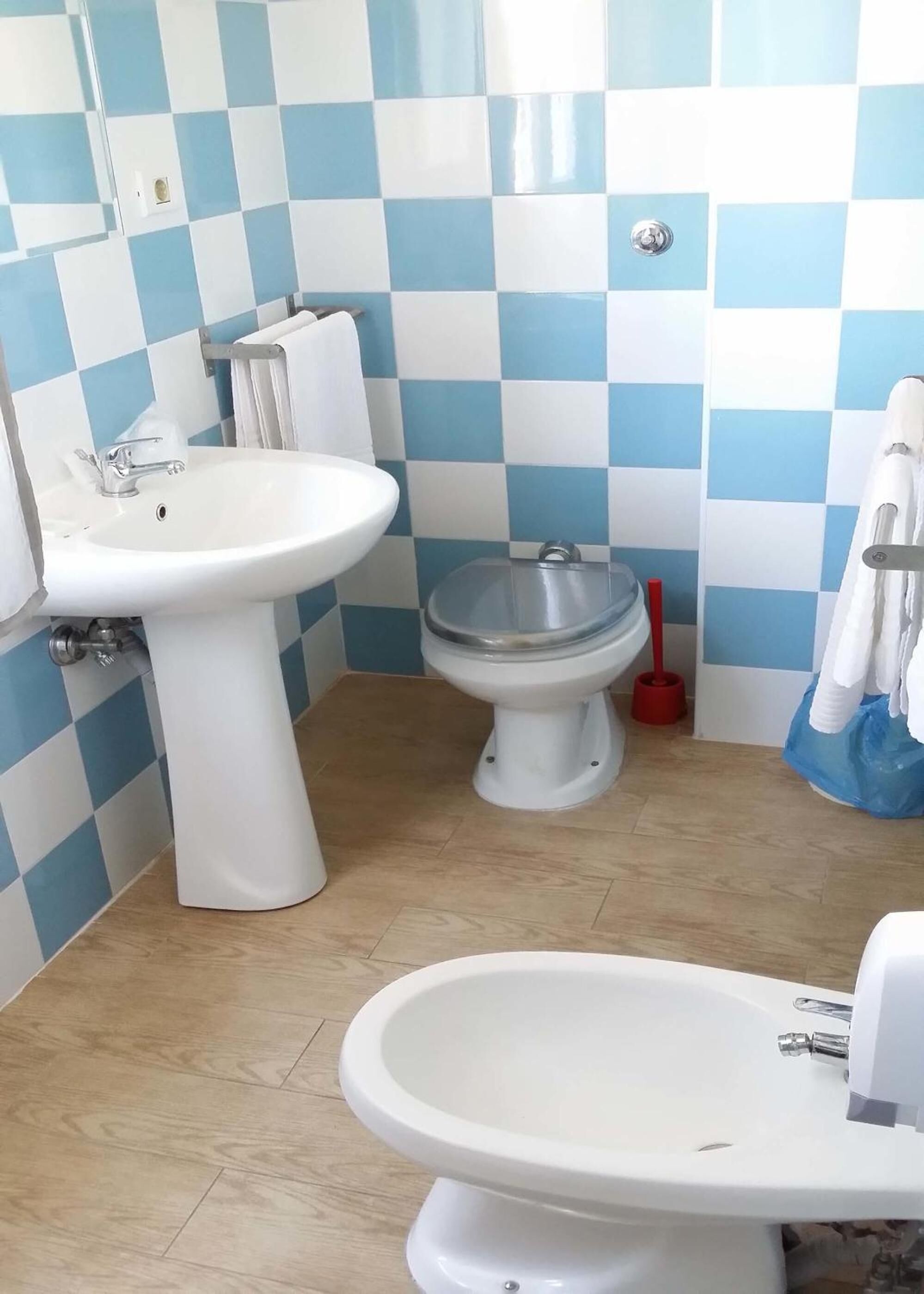 A bathroom with a sink, toilet, and bidet. The walls are tiled in a blue and white checkered pattern.