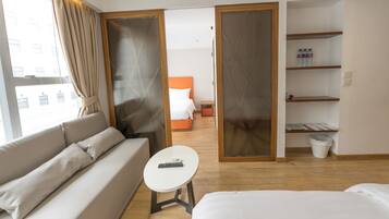 Moderni hotellihuone, jossa on sohva, pieni pöytä, sänky, näkymä toiseen huoneeseen ja hylly, jossa on pulloja.