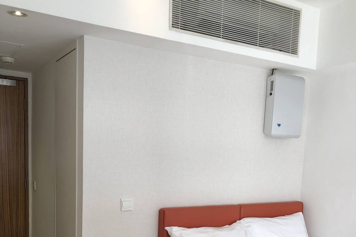 Ein Schlafzimmer mit einem Bett, einem Nachttisch, einem Holzschrank, einem Lüftungsgitter und einer Wand-Klimaanlage.