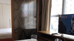 A hotel room with a dining table set for two, a TV displaying 'Same Day' and 'The Blacklist 6', and a view of the city through the window. - Homy Residence (Kowloon)
