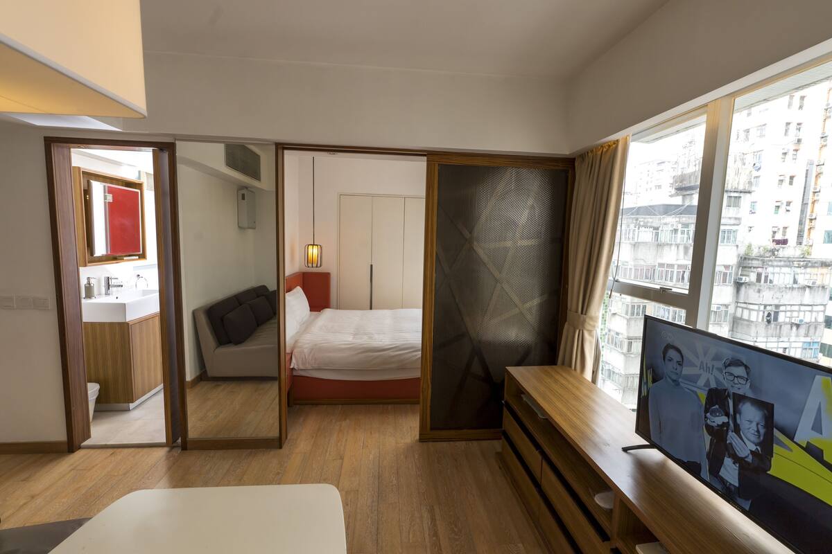 Ein Hotelzimmer mit Bett, Fernseher, Schreibtisch und Fenster mit Blick auf die Stadt.