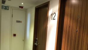 A hallway with two doors, one marked with the number 12, and a fire hose reel sign on the wall. - Homy Residence (Kowloon)