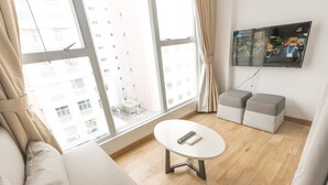 A modern living room with a large window, a flat-screen TV mounted on the wall, a round coffee table, and a sofa. - Homy Residence (Kowloon)
