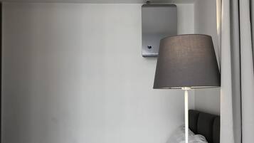 Hotellihuone, jossa on sänky, seinään asennettu ilmastointilaite, lamppu ja ikkuna, jossa on verhot.