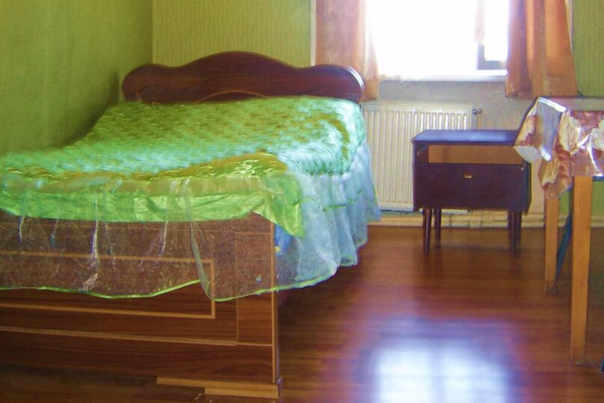 Une pièce comprenant un lit, un radiateur, une table et une fenêtre avec des rideaux.