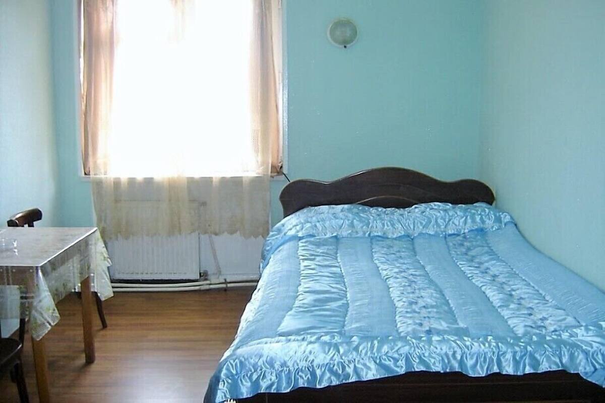 Une chambre avec un lit simple, une table et une fenêtre avec des rideaux.