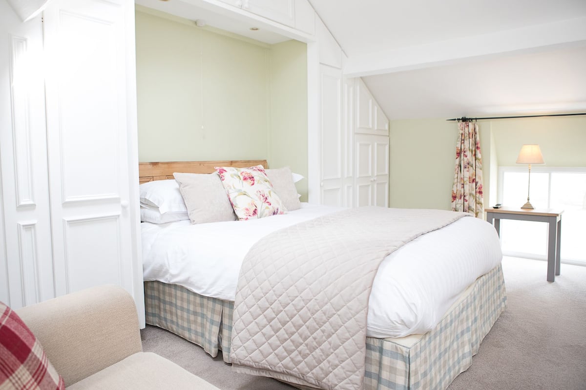 A bedroom with a bed, a nightstand, a chair, and a window with curtains.
