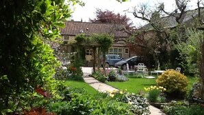 A garden pathway leading to a building with a tiled roof, surrounded by lush greenery and flowering plants.