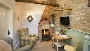 A cozy room with a fireplace, a television mounted on the stone wall, and a dining area with a table and chairs.