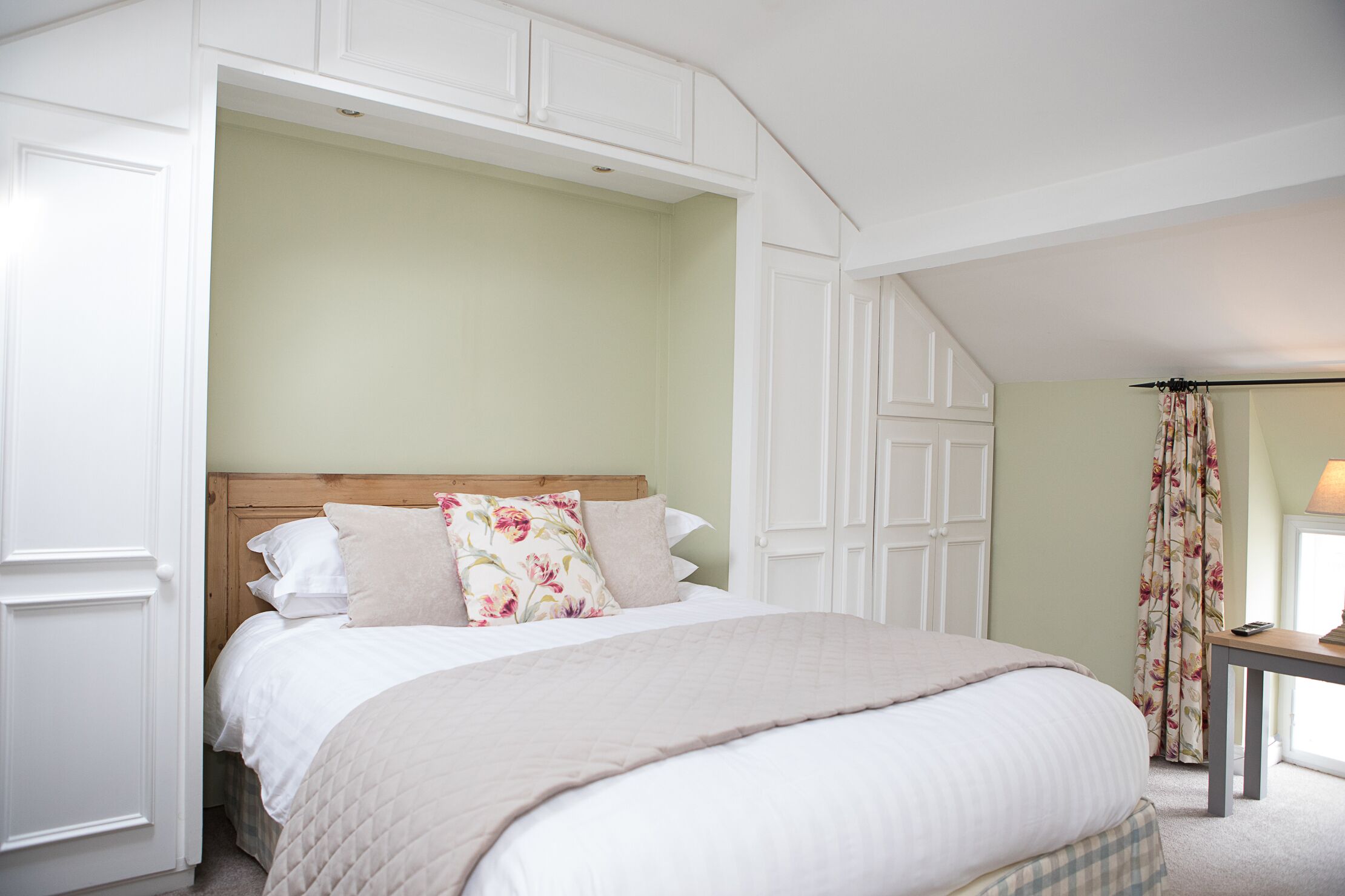 A bedroom with a large bed, a wooden headboard, and a window with curtains.