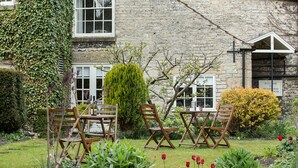 A stone building with ivy, a garden with red tulips, and wooden chairs and tables.