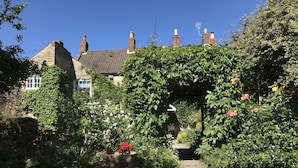 A garden with a stone wall, a gravel path, and a house with a tiled roof and chimneys.