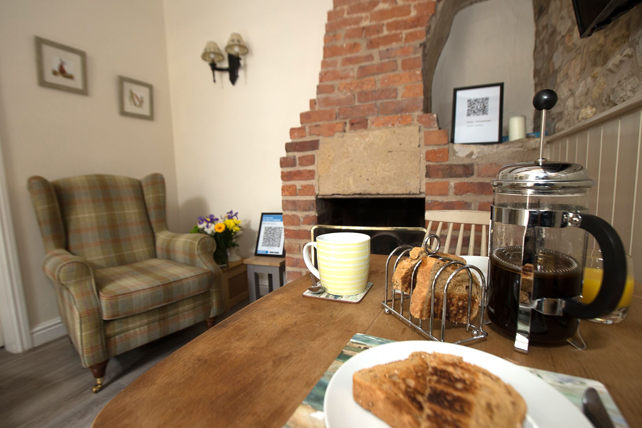A cozy room with a plaid armchair, a coffee table with a mug, a bread rack, and a coffee maker.