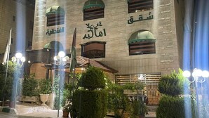 A building with multiple windows, some with green awnings and others with wooden shutters. There are potted plants in front of the building. - Amaled Hotel (Amman)