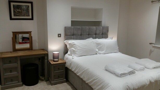 Une chambre à coucher avec un lit, des tables de chevet, une lampe, un tableau encadré et une poubelle.