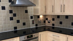 Une cuisine moderne avec des meubles de couleur bois clair, des plans de travail noirs et une hotte en acier inoxydable.