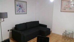 Un salon avec un canapé noir, une table en verre et deux tableaux abstraits accrochés au mur.