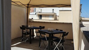 Un patio al aire libre con mesa y sillas, un toldo color beige y vista de edificios al fondo.
