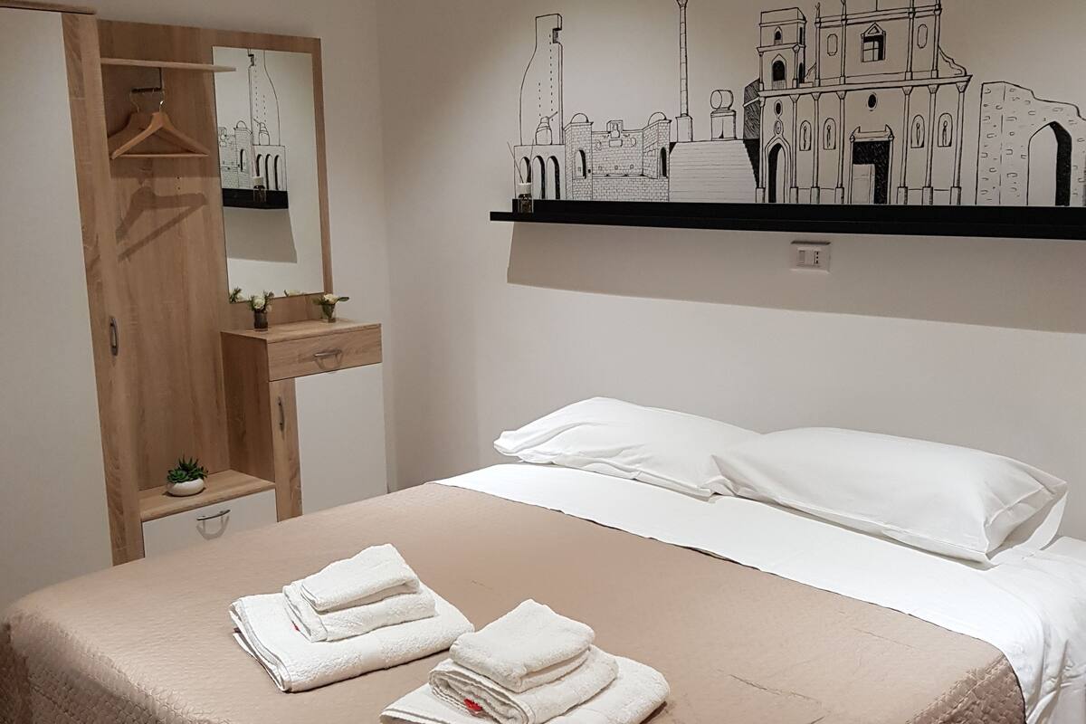 A neatly made bed with a beige quilt, two white pillows, and folded towels on the bed.