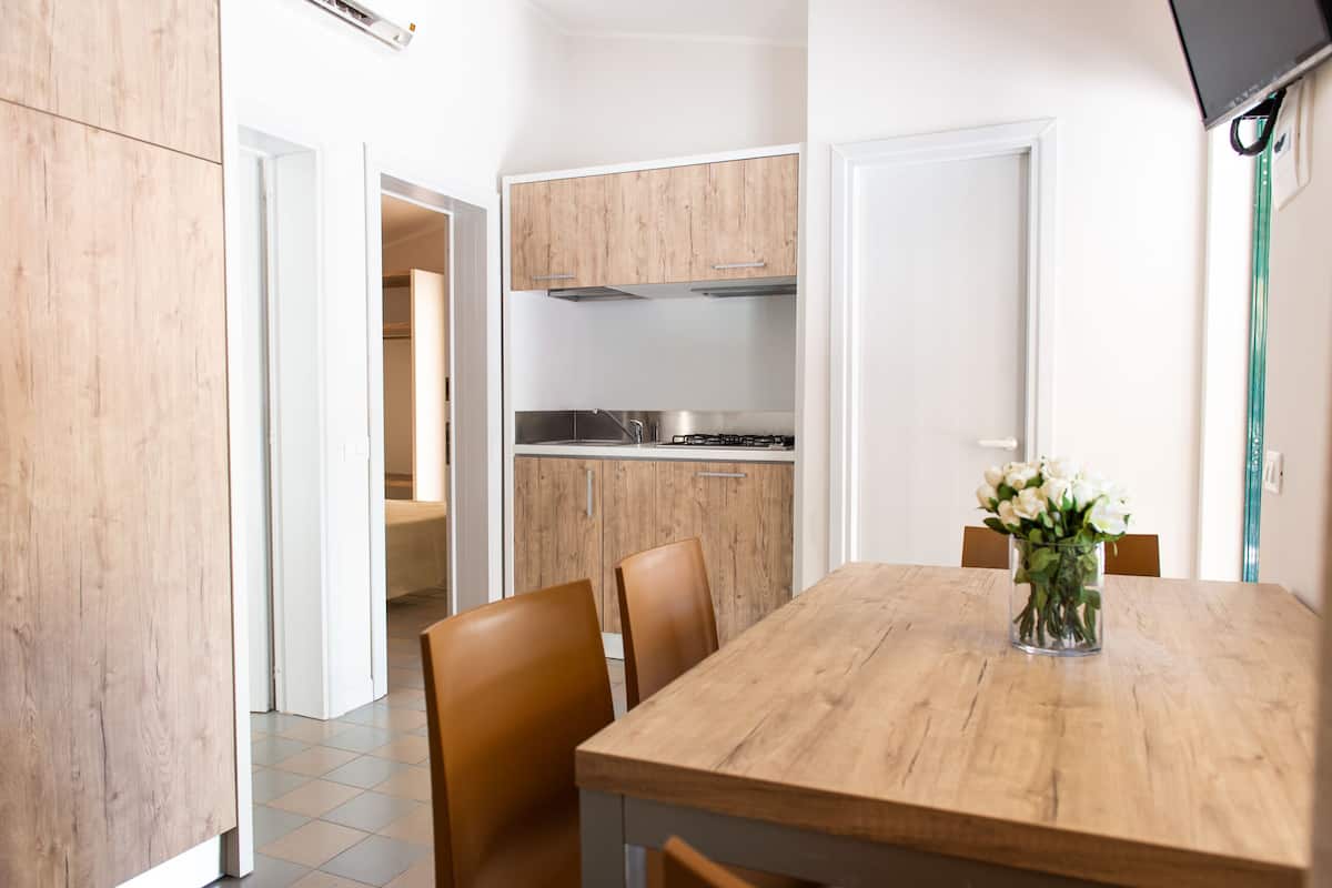 A modern kitchen with wooden cabinets, a stainless steel stove, and a dining area with a wooden table and chairs.