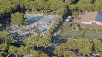 An aerial view of a resort with multiple swimming pools, sun loungers, and a tennis court.