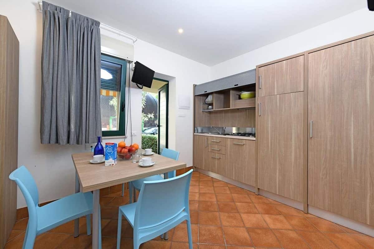 A compact kitchen with a dining table, chairs, and a TV mounted on the wall.