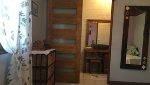 A bedroom with a wooden wardrobe, a bedside table with a decorative item, a mirror, and a view into the bathroom. - La Caz Océane (Saint-Leu)