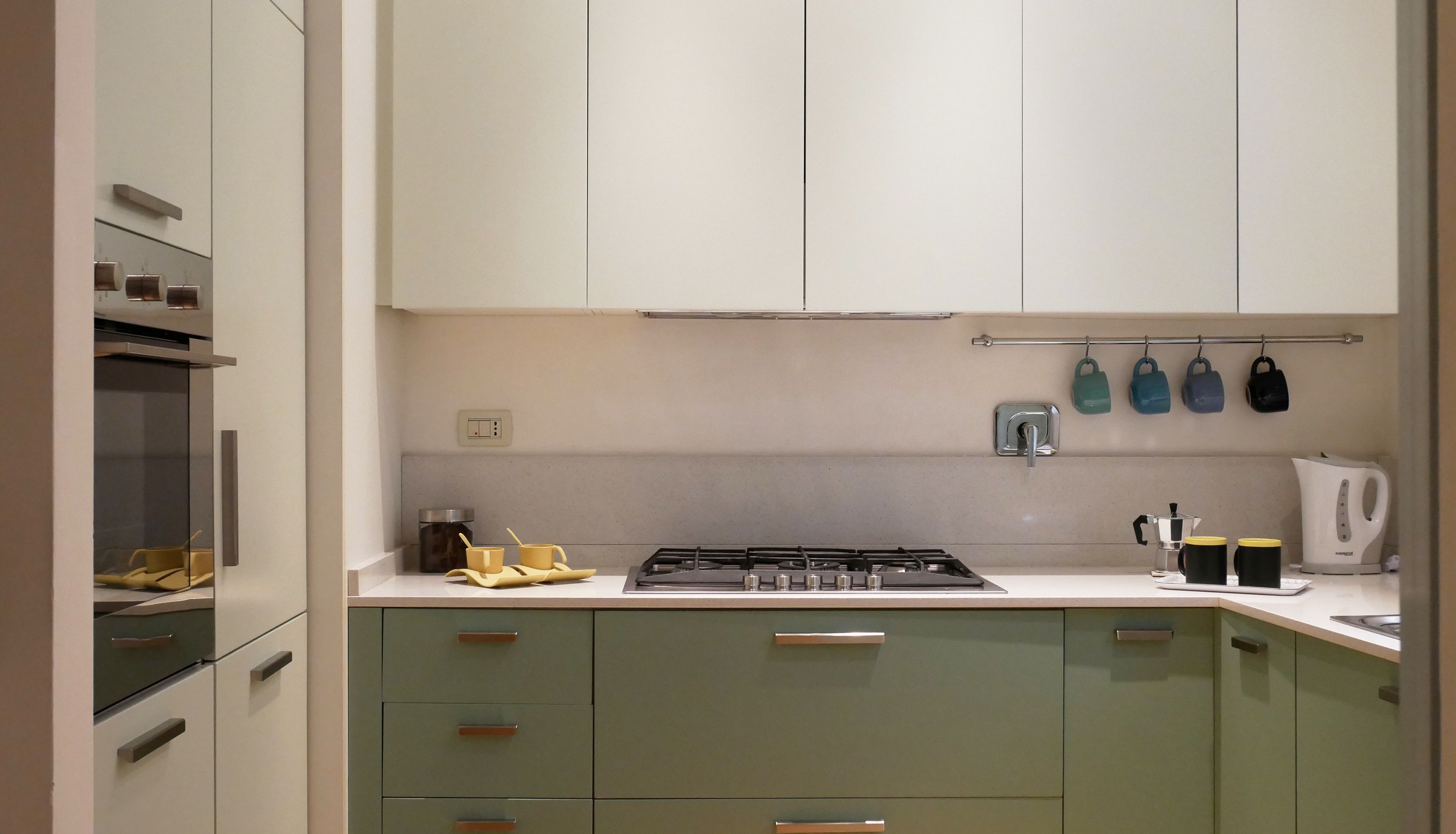 A kitchen with a stove, sink, and cabinets. There are mugs and a kettle on the counter.