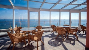 A sunlit deck with wicker furniture and a glass ceiling overlooking the ocean. - Sirius Beach Hotel & SPA (Varna)