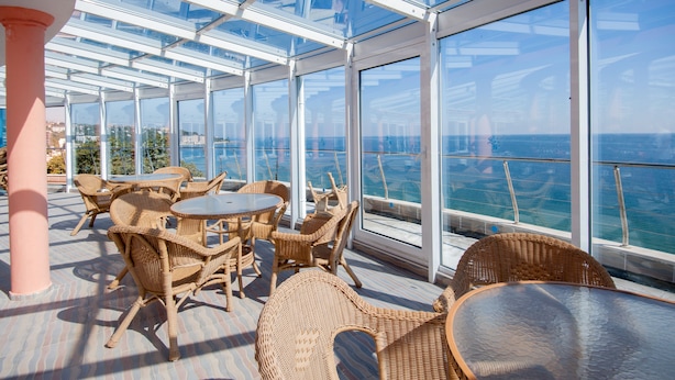 A glass-enclosed outdoor area with wicker furniture and a view of the sea. - Sirius Beach Hotel & SPA (Varna)