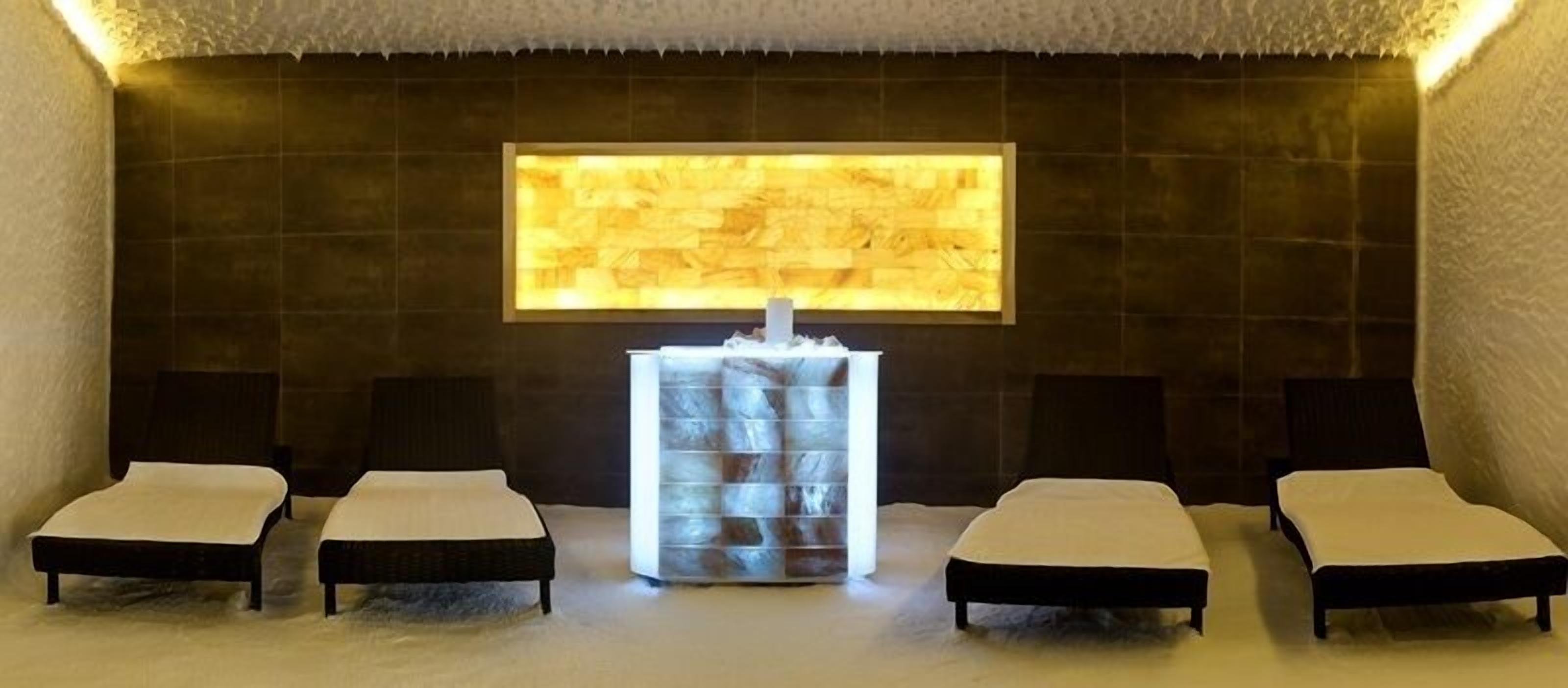 Uma sala de spa com três camas, um elemento central de água e uma grande parede iluminada.