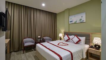 A hotel room with a bed, two chairs, a desk, and a painting on the wall.