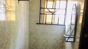 Une petite salle de bain carrelée, avec des toilettes, une fenêtre grillagée et un miroir.
