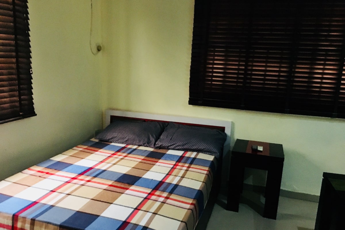 A bedroom with a bed, a nightstand, and a window with blinds.