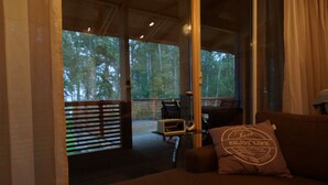 Ein gemütlicher Wohnbereich mit einer Couch, einem Couchtisch und einem Fenster mit Blick auf eine Terrasse und einen Wald.
