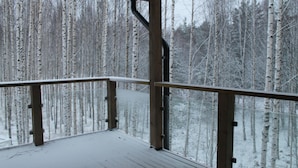 A wooden deck with a metal railing overlooking a snowy forest.