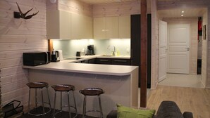 A modern kitchen with a bar area, wooden walls, and a door leading to another room.