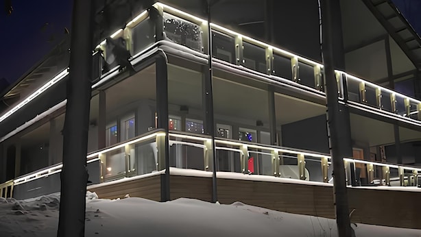 A modern, multi-story building with glass railings and illuminated railings, surrounded by snow.