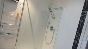 Un área de ducha moderna con mampara de vidrio, cabezal de ducha de mano y grifo empotrado en la pared.