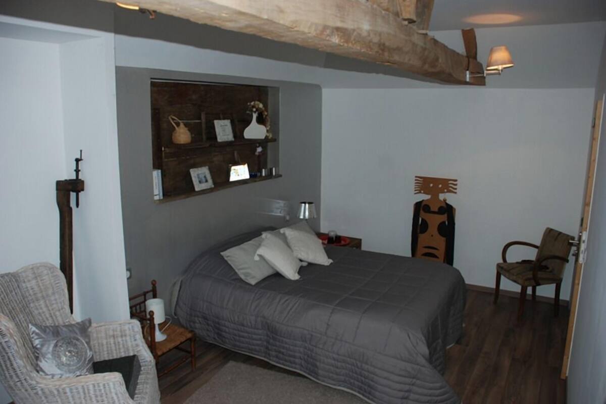 A bedroom with a large bed, a chair, a shelf with decorative items, and a lamp.