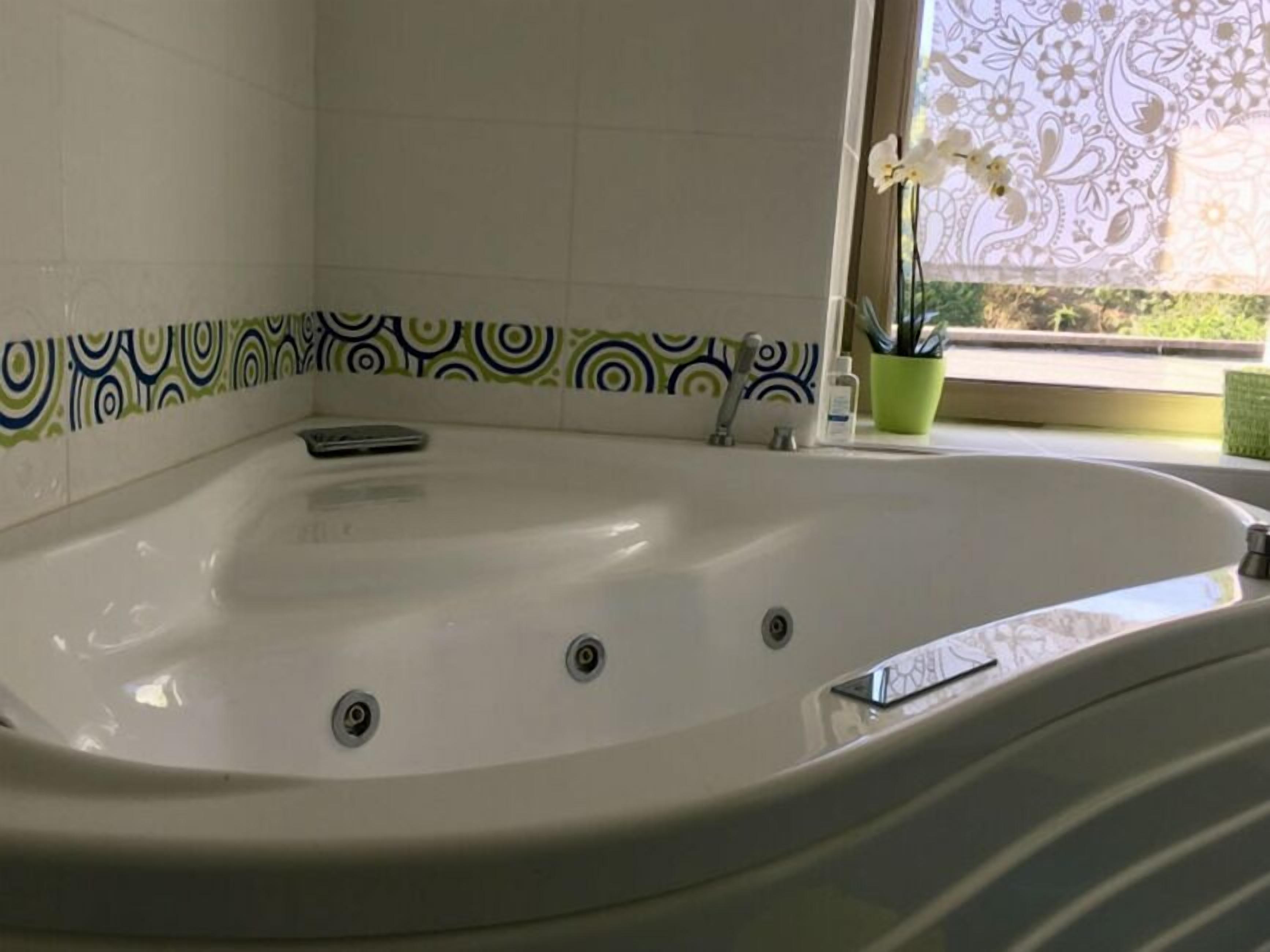 Ein Badezimmer mit einer großen Badewanne, einem Fenster mit Ausblick und einer Wandfliese mit Muster.