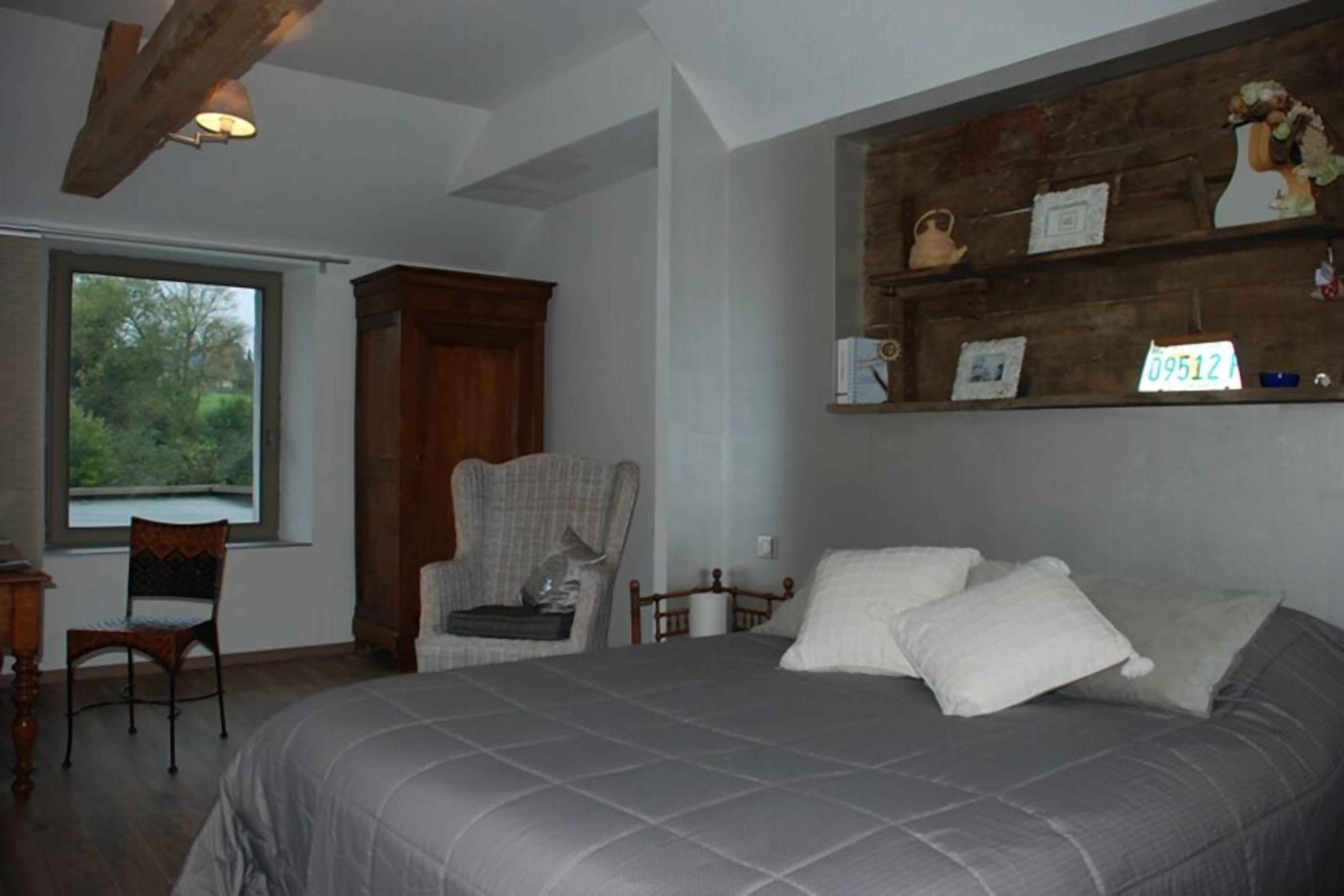 Un dormitorio con una cama grande, una silla de madera, un escritorio y una ventana con vistas a zonas verdes.