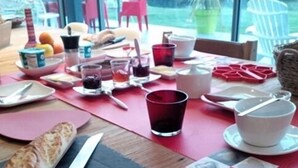 Una mesa de desayuno con pan, un cuchillo, una taza roja y diversos alimentos para el desayuno.