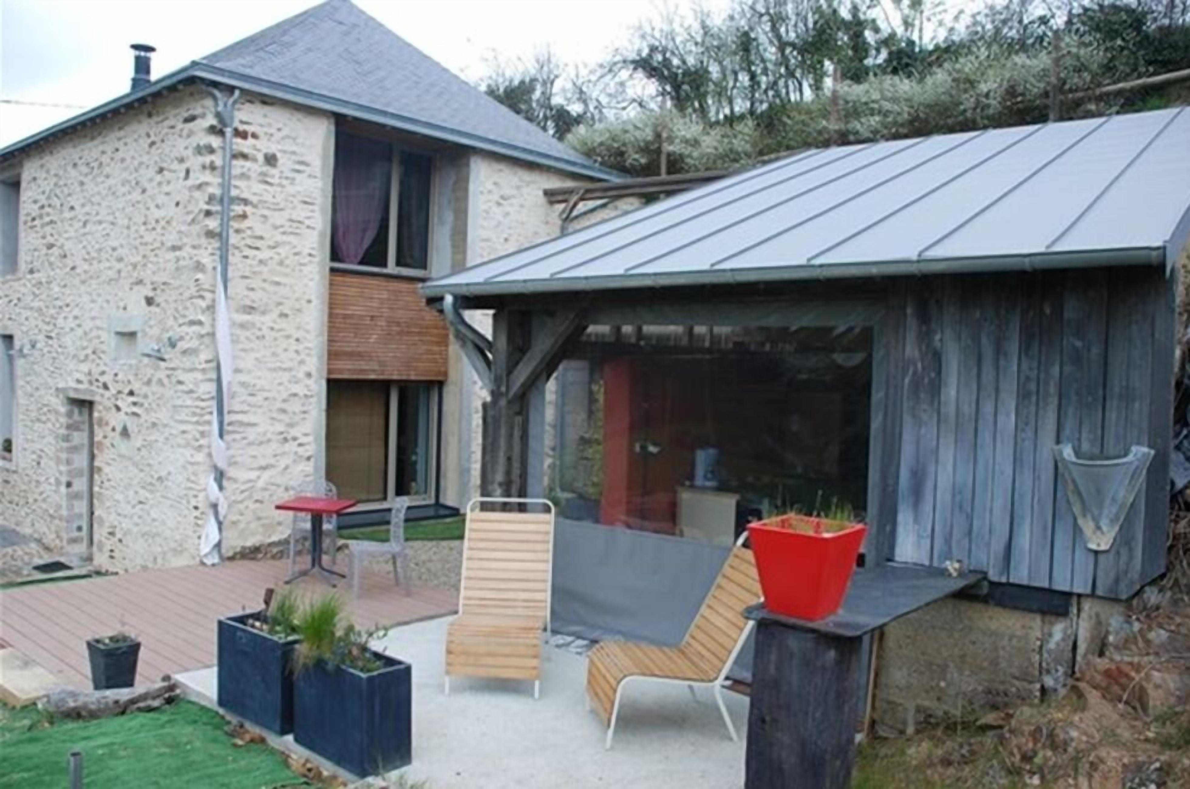 A stone house with a metal roof, a wooden deck, and outdoor seating.
