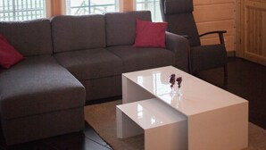 A room with a wooden interior, a gray sofa, a red pillow, a white coffee table, and a chair. - SResort Sauna Villas (Lappeenranta)